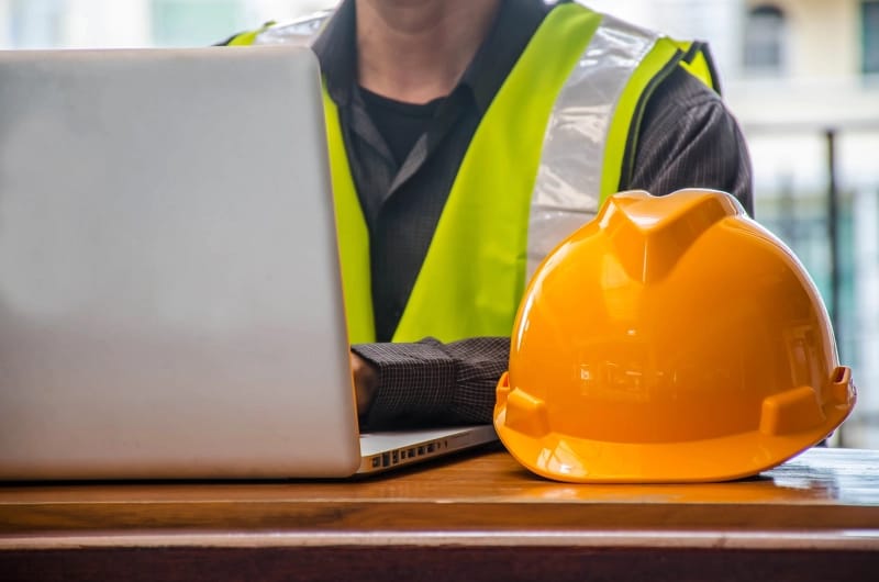 Żółty kask ochronny i biznesmen w branży budowlanej pracują przy komputerze w tle