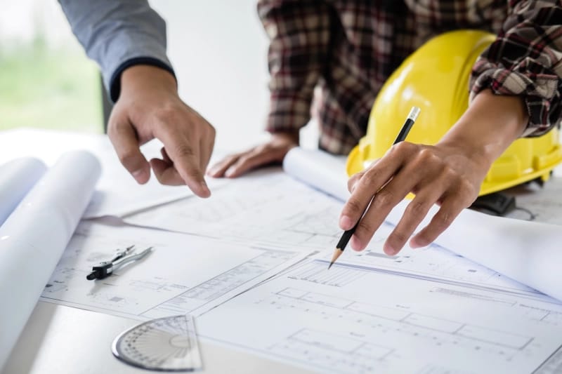 Inżynierowie budownictwa lub architekci omawiają projekt, sprawdzając informacje na rysunkach i szkicach podczas spotkania w celu realizacji projektu architektonicznego na placu budowy